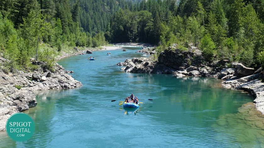 People white water rafting on a clear turquoise river surrounded by forest and mountains, representing adventure tourism and outdoor experiences.